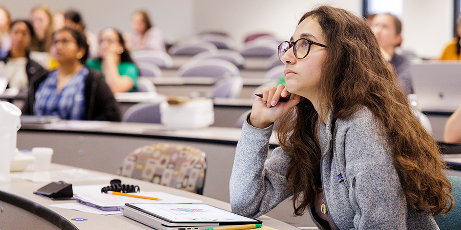 A college student attentively listening during a lecture in a tiered classroom.