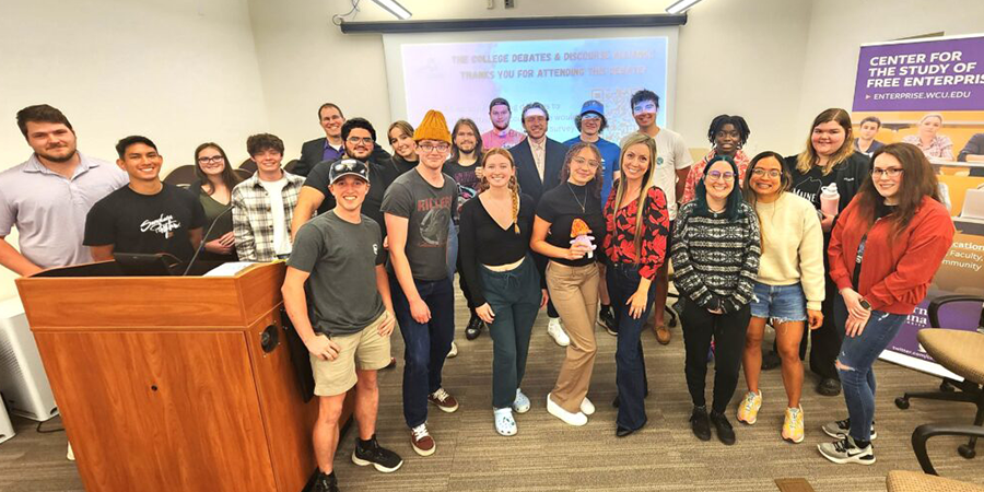 A diverse group of students and adults posing in a classroom beside a wooden podium. 