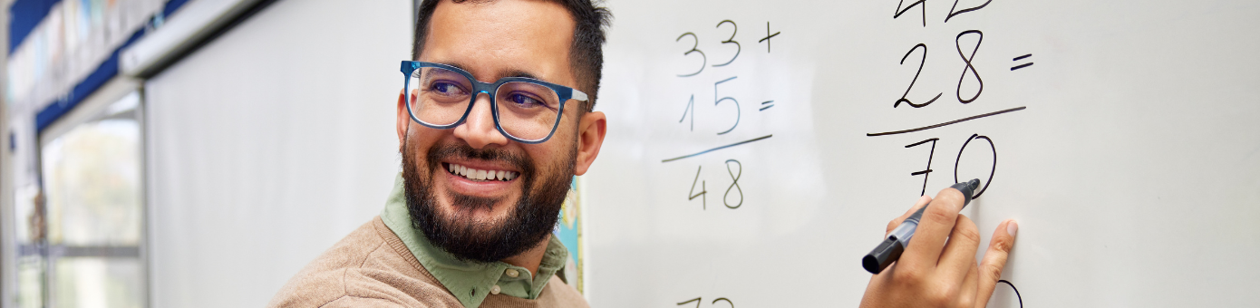 Male teacher smiles while writing math equations on a whiteboard
